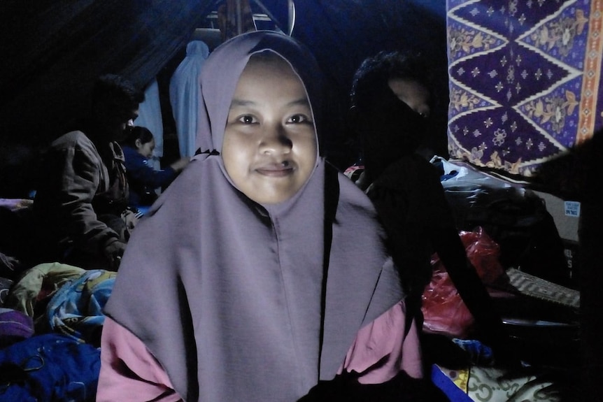A woman wearing headscarf smiling at camera in a dark shelter.