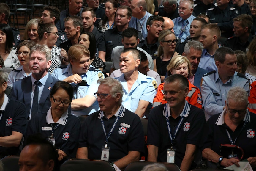 Men and women, many dressed in emergency service uniforms, are seated at the memorial service.