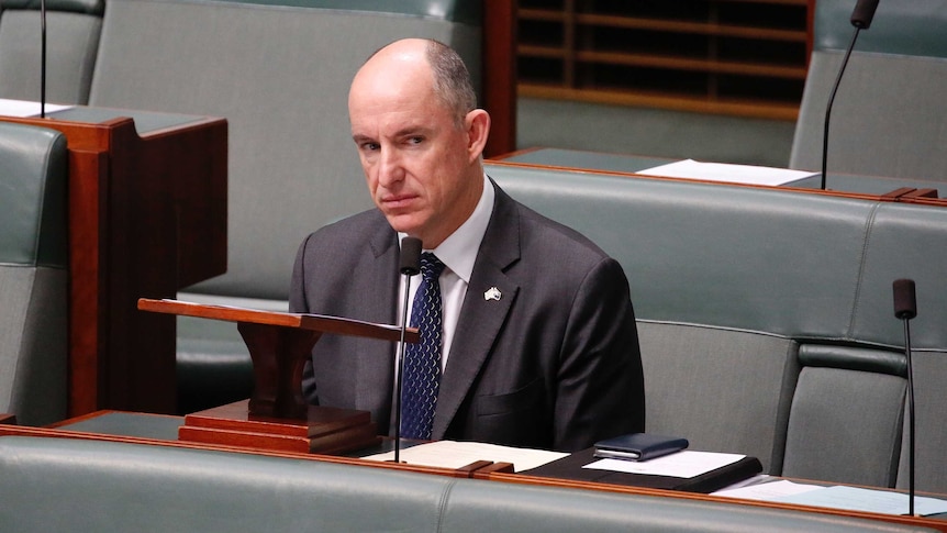 Robert is looking out the corner of his eye towards the speaker's chair. He's wearing a blue tie and an Australia pin.