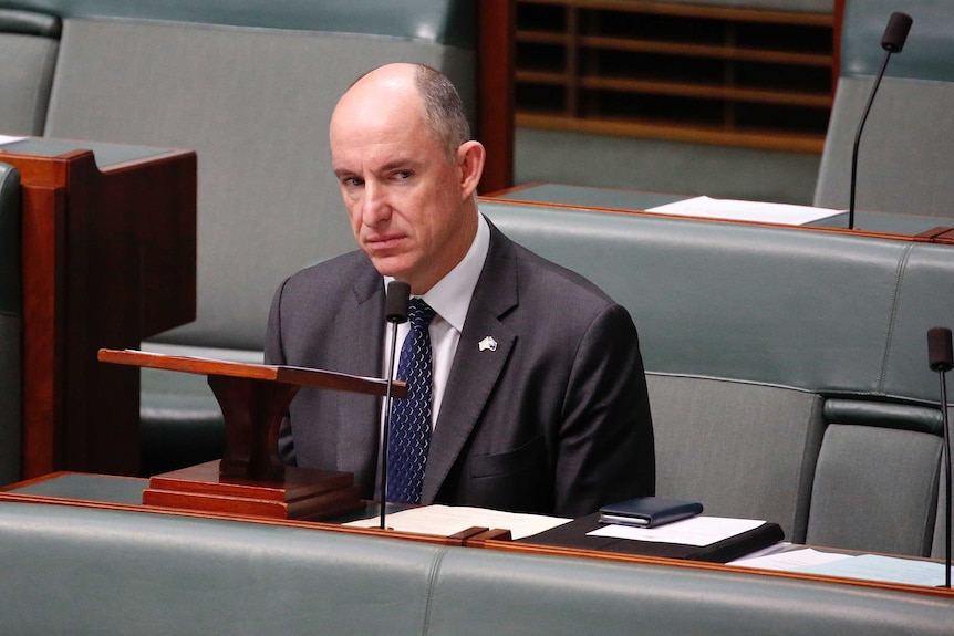 Robert is looking out the corner of his eye towards the speaker's chair. He's wearing a blue tie and an Australia pin.