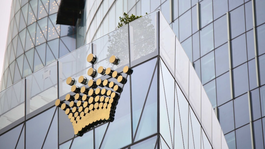 A gold coloured Crown logo on the glass casino sky scraper in Baranagaroo, Sydney on an overcast day