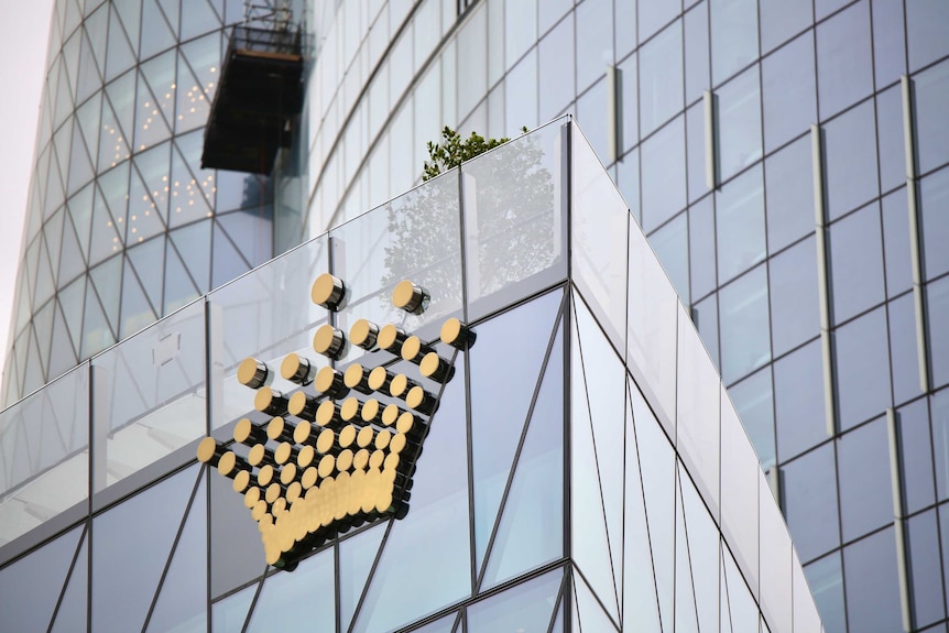 A gold coloured Crown logo on the glass casino sky scraper in Barangaroo, Sydney on an overcast day
