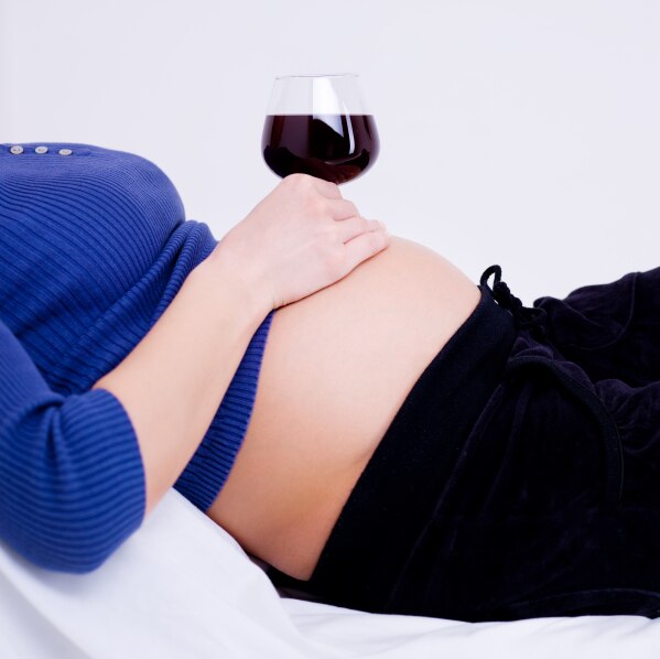 Pregnant woman with a glass of red wine sitting on her belly