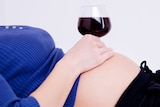 Pregnant woman with a glass of red wine sitting on her belly