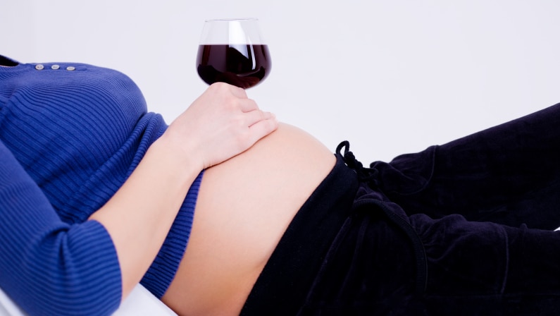 Pregnant woman with a glass of red wine sitting on her belly