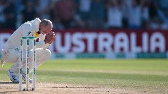 A cricketer crouches down with his arms resting on his knees after an Ashes Test loss.