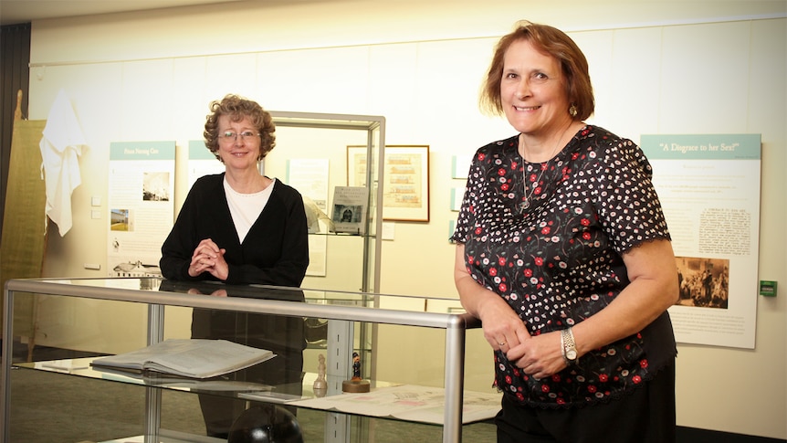 Louella McCarthy and Kath Weston lean on a display cabinet at the Caring for the Incarcerated exhibition.