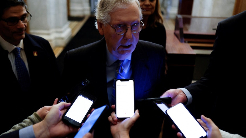 Reporters illuminate Mitch McConnell's face as they point their smartphones towards his face