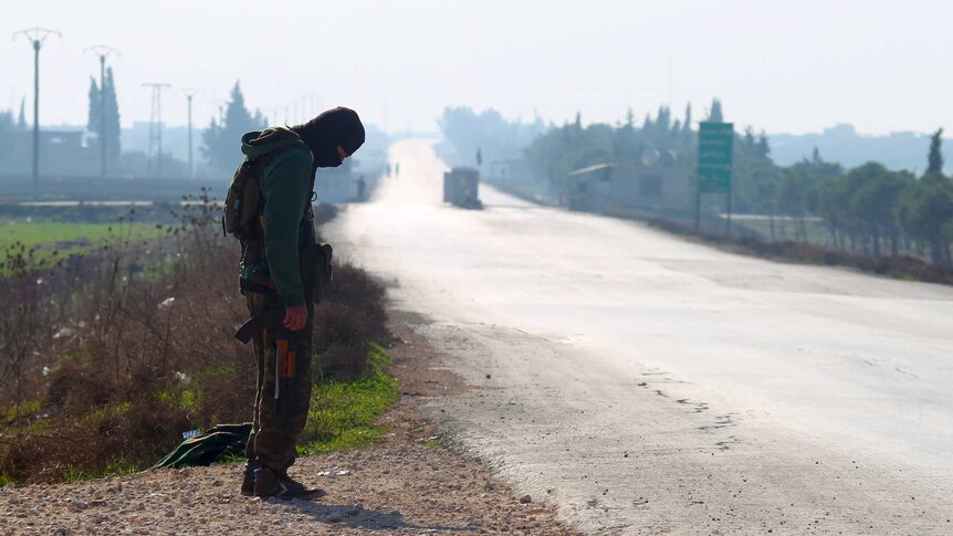 A Syrian rebel fighter secures a road waiting for a convoy of fighters and civilians to pass.