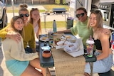 Five women sit around a table outside a caravan