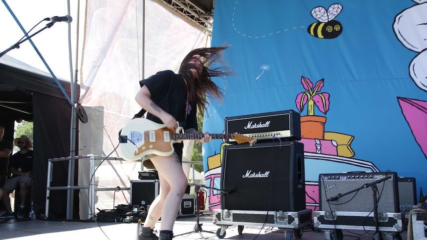 Woman on stage playing guitar she's shaking her head and her hair is flying everywhere