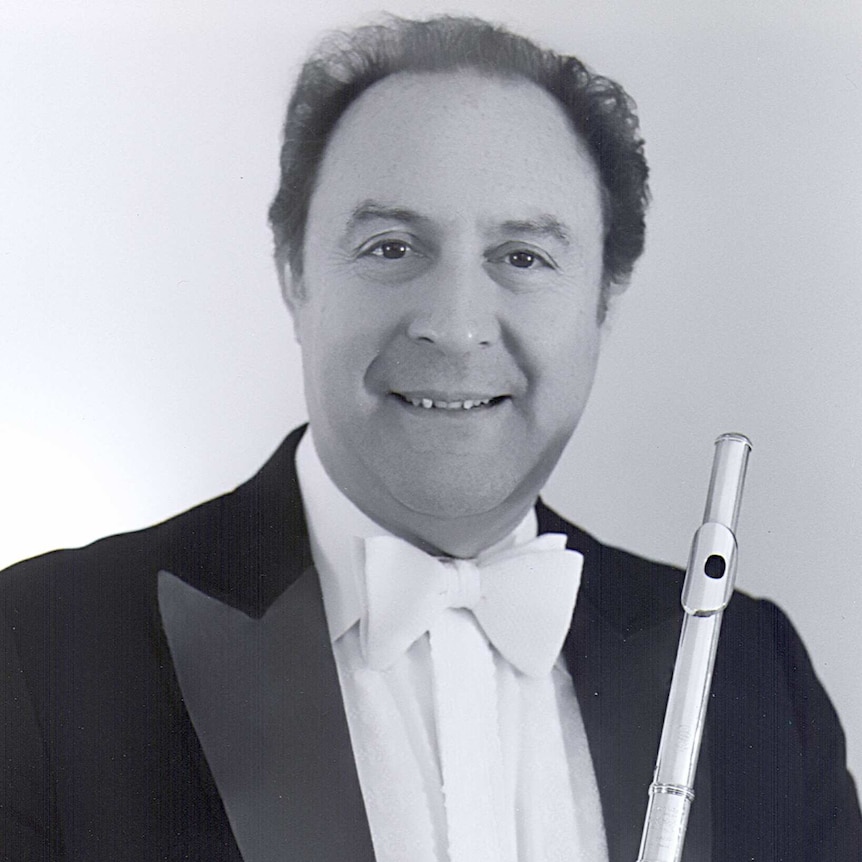 A black and white image of a man in a tuxedo holding a flute.