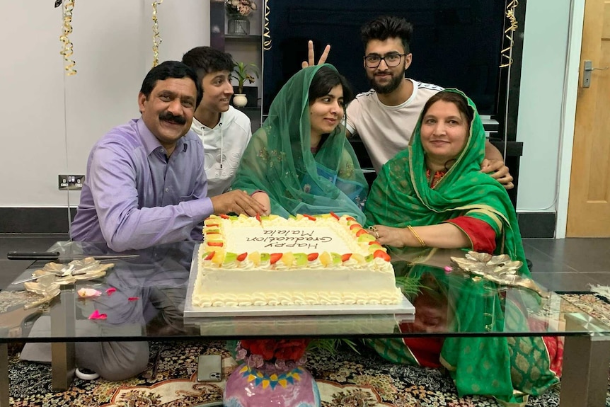 Malala Yousafzai and her family sit around a large cake.