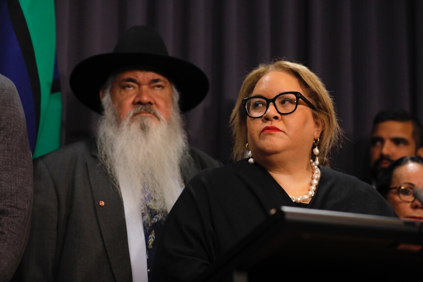 Professor Megan Davis looks off camera standing at a lectern, with Labor MP Pat Dodson visible behind her.