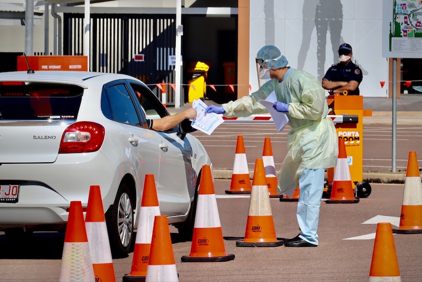 A person in full PPE is at a testing site as a car drives past