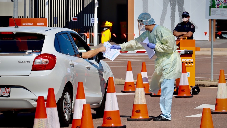 A person in full PPE is at a testing site as a car drives past