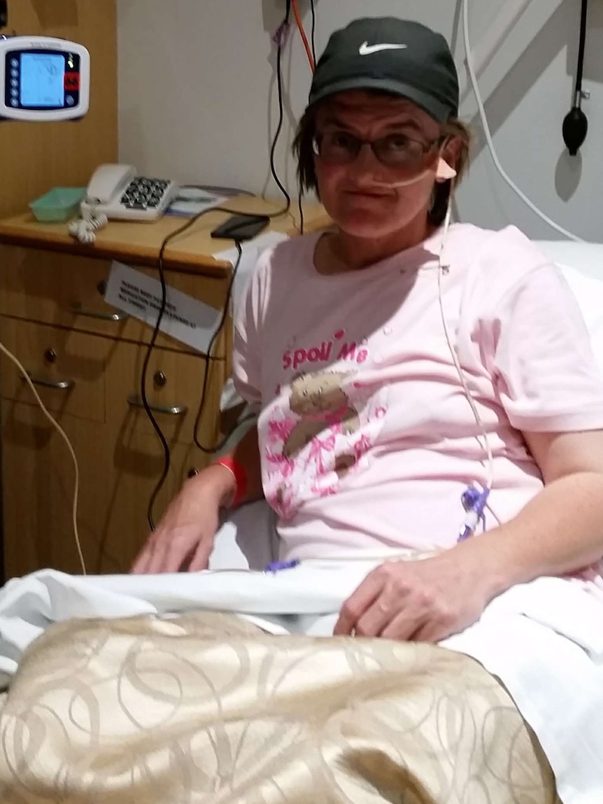 A woman in a cap sits up in a hospital bed with a tube attached to her nose.