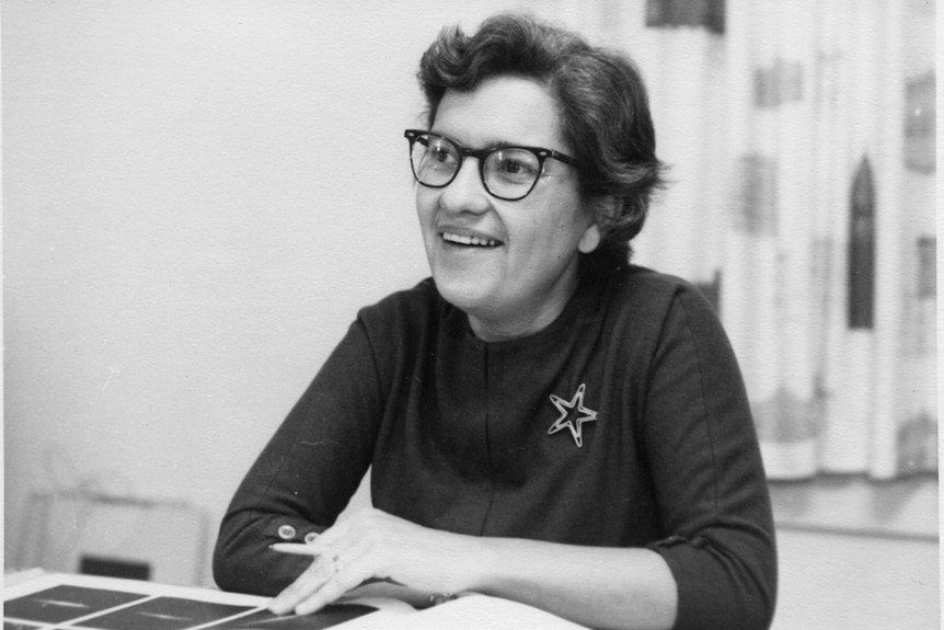 A black and white photo of a woman, Vera Rubin, sitting at a table.