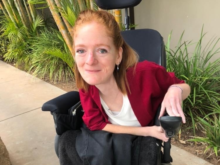 Zia Westerman sits outside in her wheelchair wearing a red cardigan and white top
