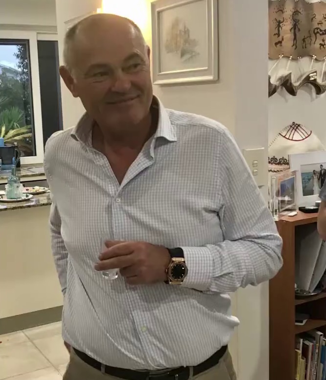 A smiling bald man in a light-coloutred, collared shirt stands in a kitchen.