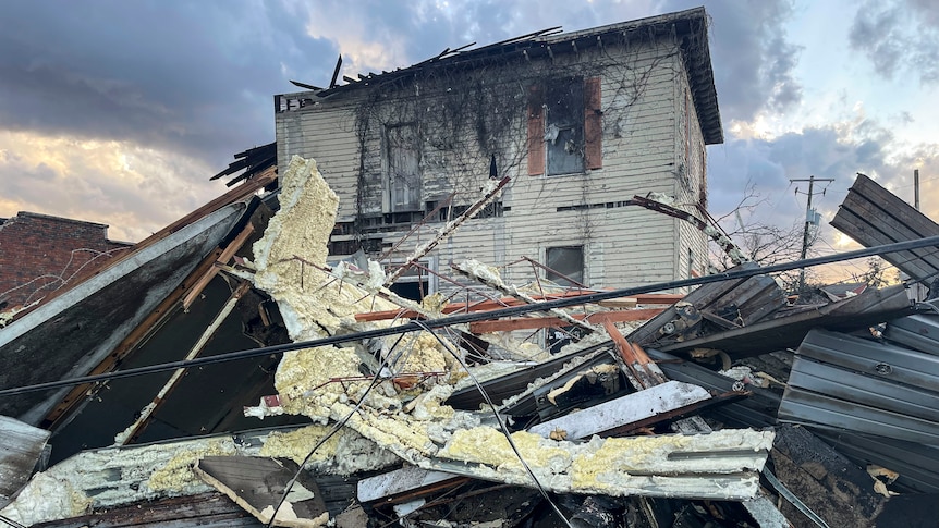 A severally damaged house with debris in front