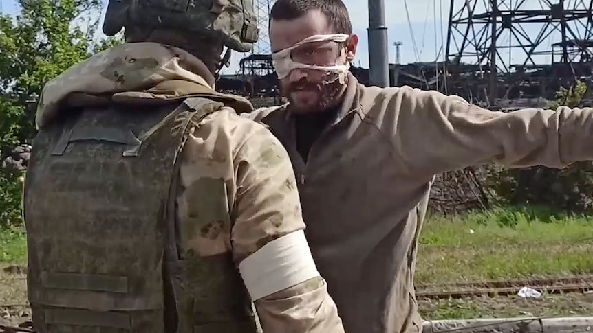 A Russian serviceman frisks a Ukrainian soldier wearing an eye patch.