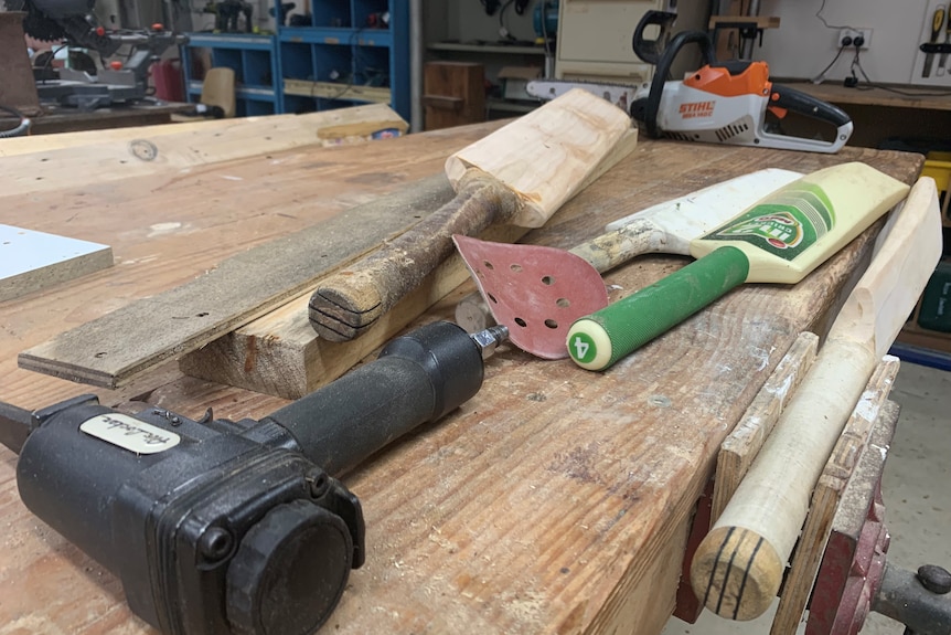 Three old cricket bats sit on a dusty workbench