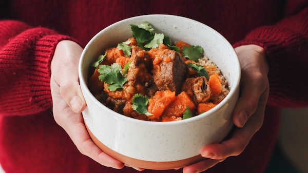 Heidi Sze's hands holding a bowl of beef, cinnamon and sweet potato stew, served over couscous for a hearty dinner for winter.