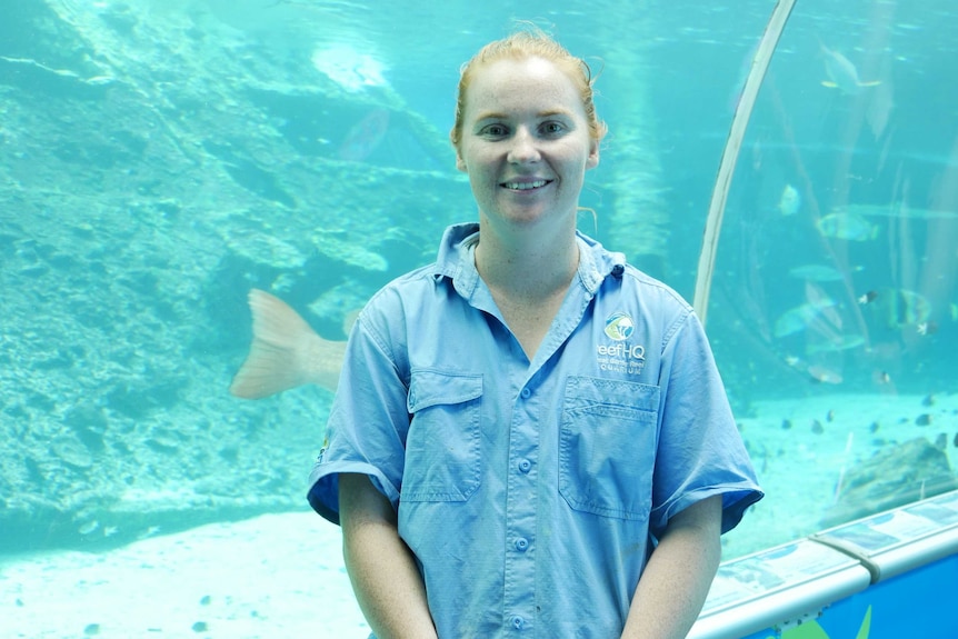 Young lady with red hair wearing light blue short sleeved button shirt standing in the underwater tunnel at reef hq