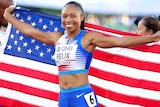 Allyson Felix smiles whlie holding an American flag behind her back