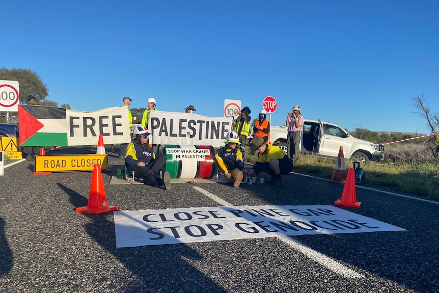 People hold a sign which reads 'close Pine Gap, stop genocide'. 