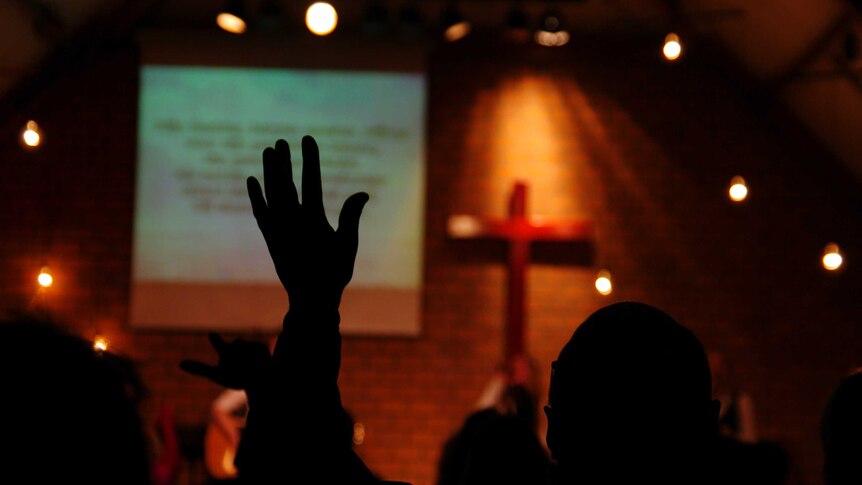 back of person with arms raised in church worship singing setting