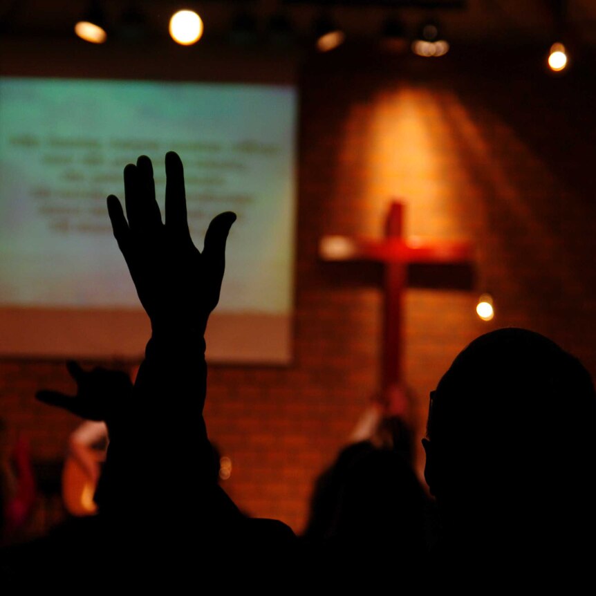back of person with arms raised in church worship singing setting