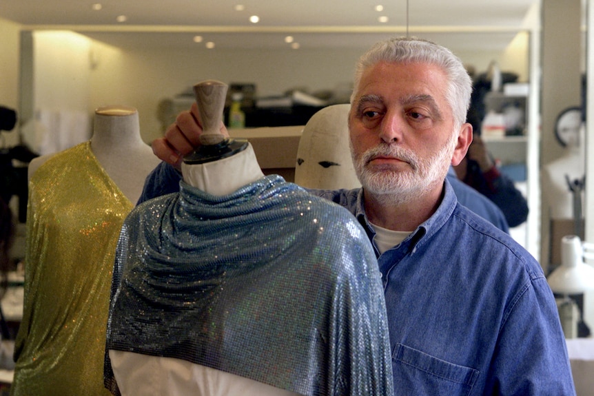 Paco Rabanne stands behind dressed mannequin in design workshop.