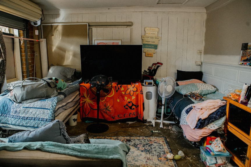 A crowded garage filled with two beds, bags, a tv, couch and other belongings. 