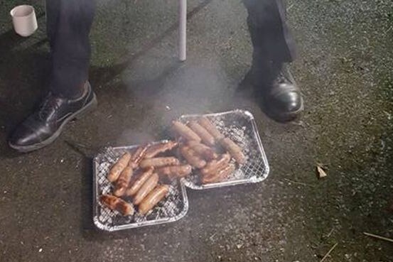 Steam rises from two foil trays full of sausages.