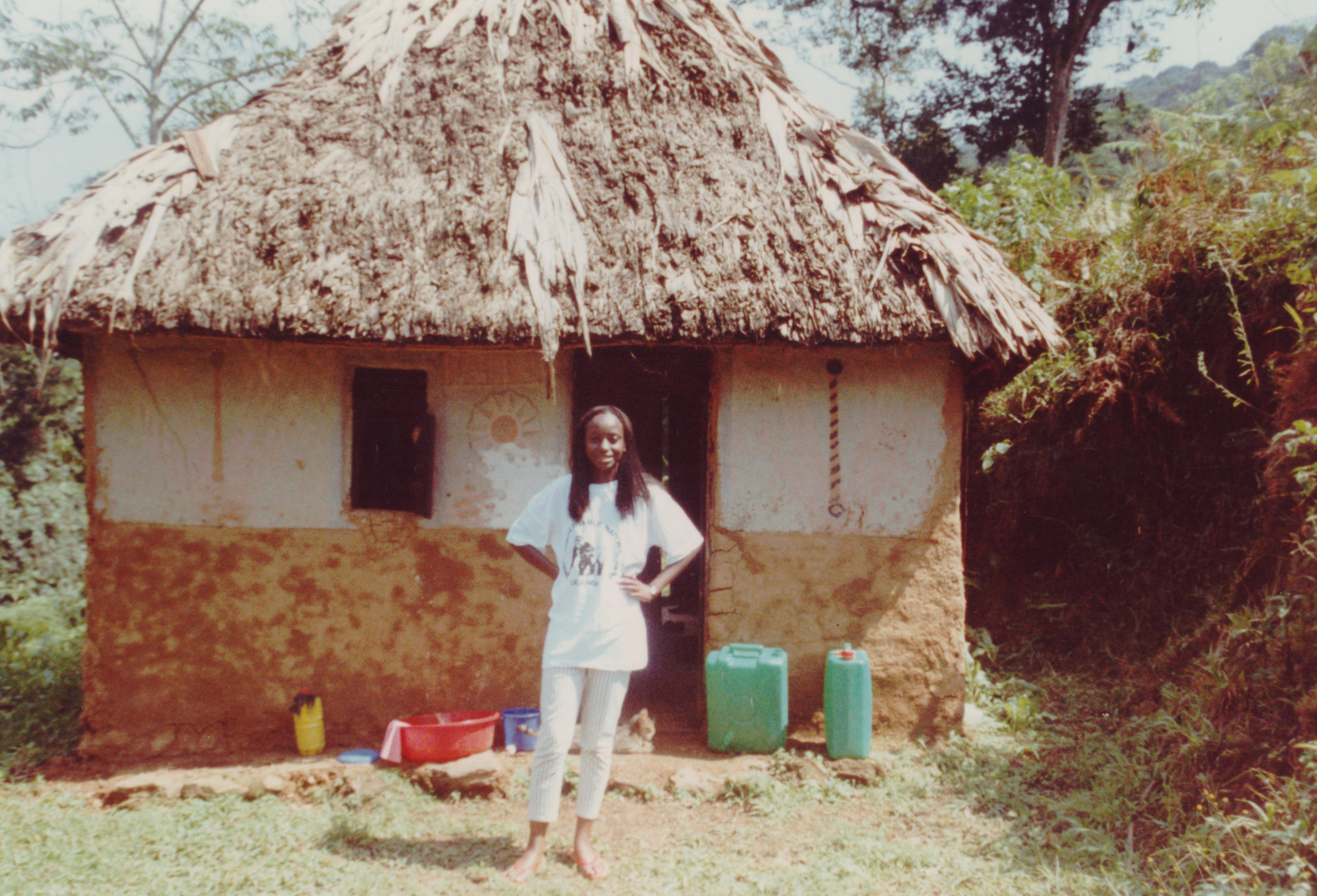 A 1990s photo of a young Ugandan woman standing in front of a mud hut