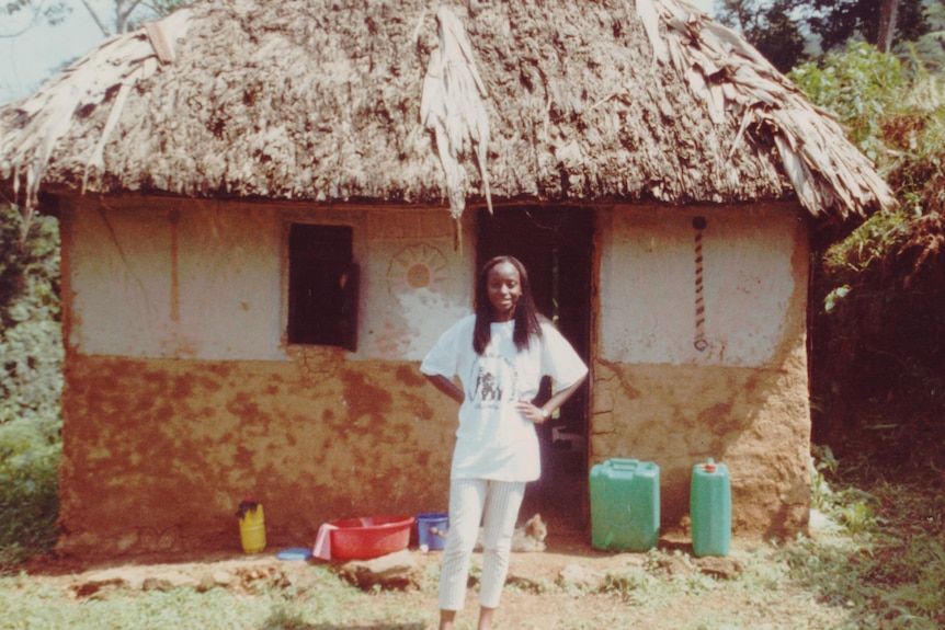 A 1990s photo of a young Ugandan woman standing in front of a mud hut