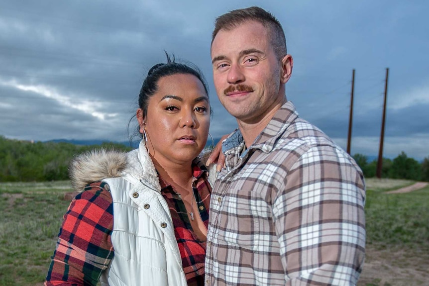 A woman rests her arm on a man's shoulder while they stand together in a field