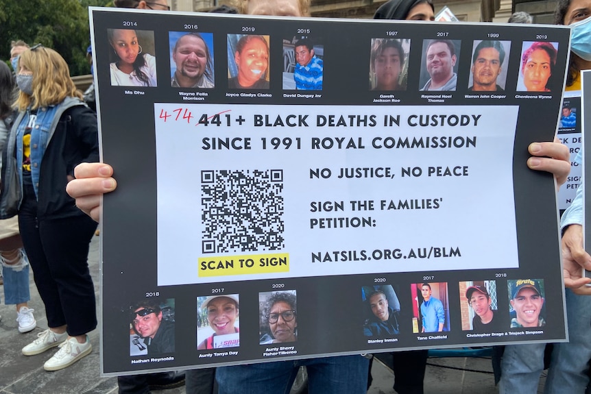 A protester holds up a sign saying "474+ Black deaths in custody since 1991 Royal Commission".