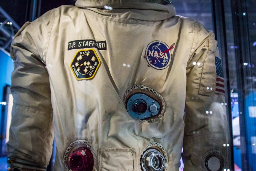 NASA space suit up-close with badges and American flag.