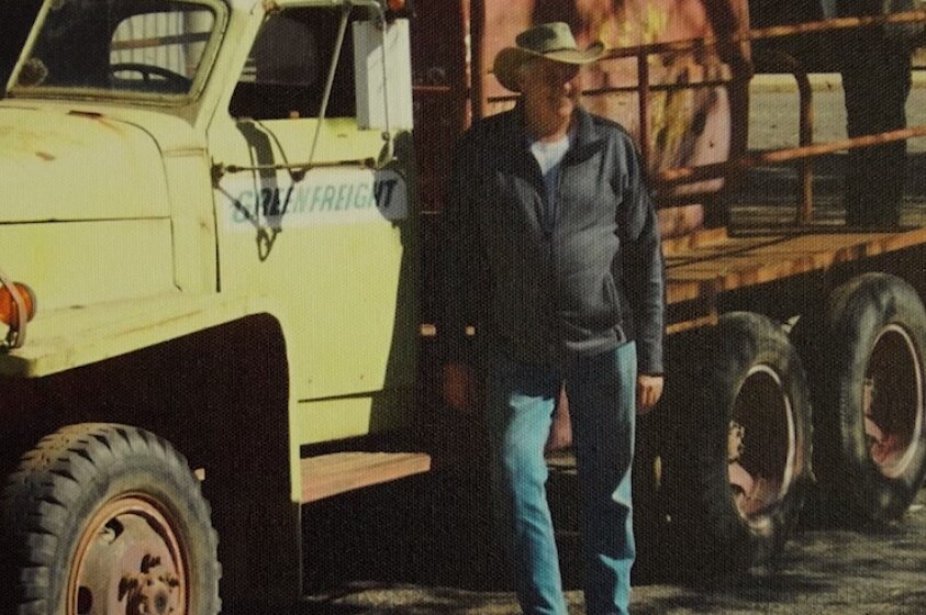 A vintage photograph of a man standing by a truck.
