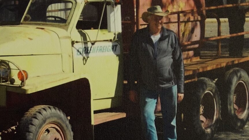 A vintage photograph of a man standing by a truck.