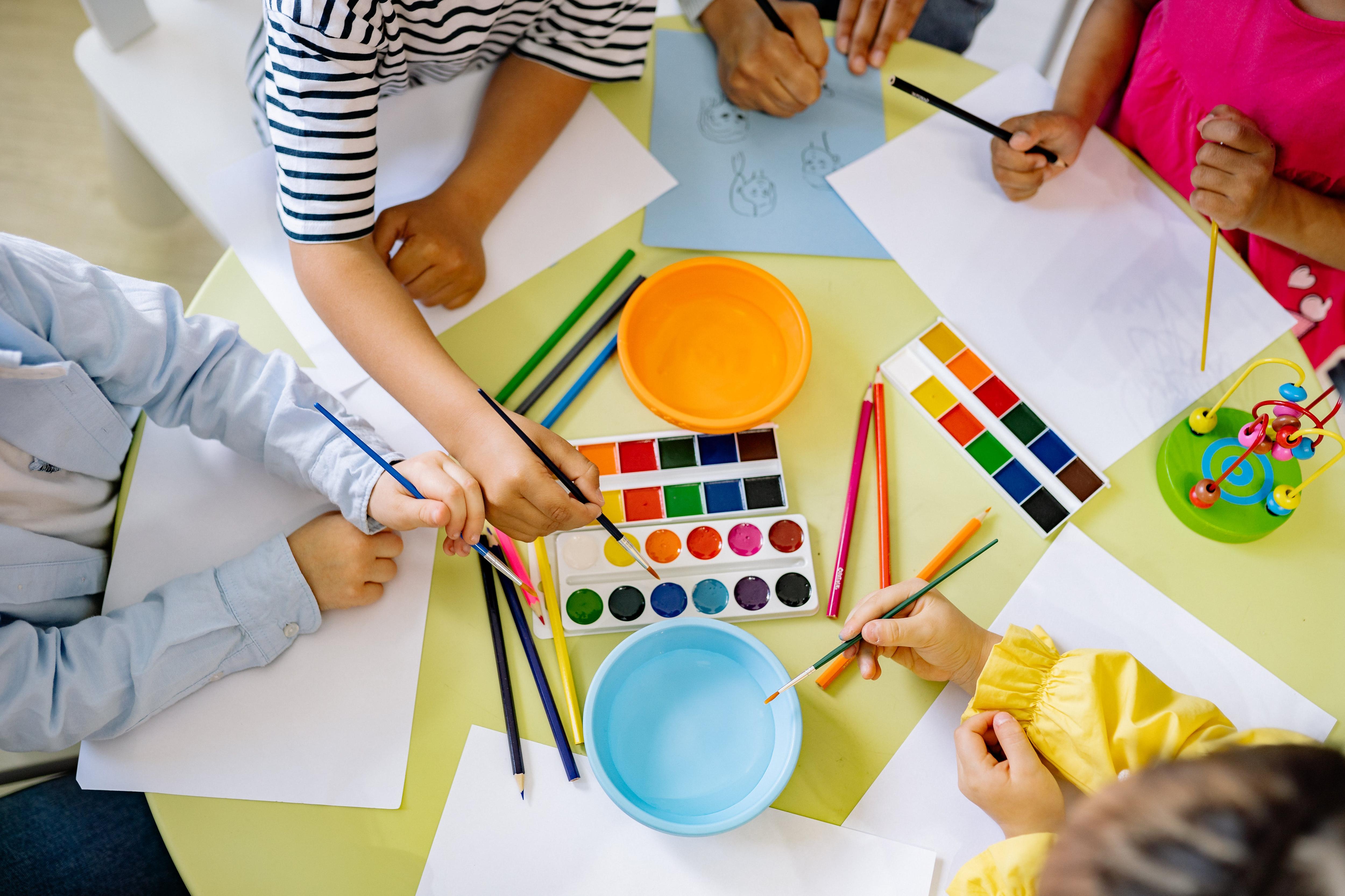 overhead shot of kids' hands about to paint on blank pieces of paper