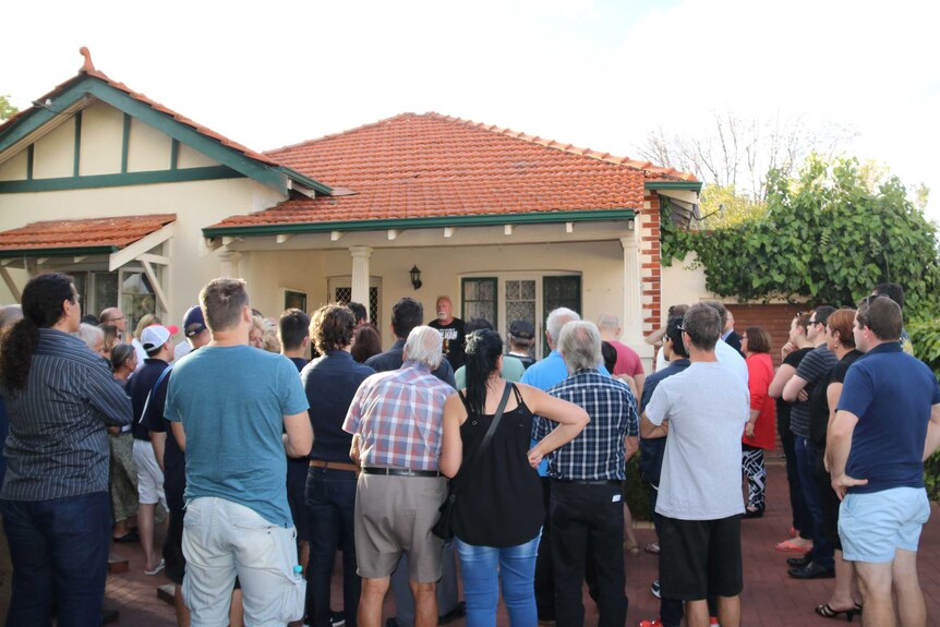 A crowd of people outside a house listening to a man speak.