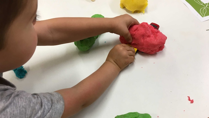 A child plays with red playdough and cars