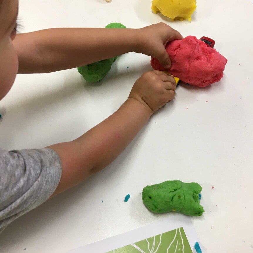 A child plays with red playdough and cars