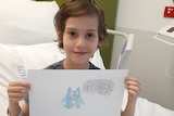 Zen holds up a drawing of Bluey from a hospital bed.