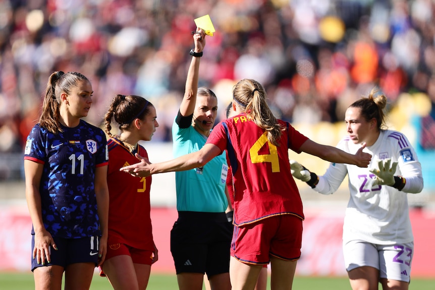 A referee holds up a yellow card, with Spain's Irene Paredes clearly unhappy 