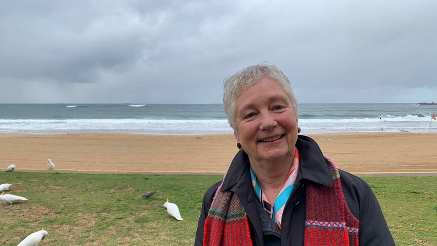 A woman, wearing a jacket and scarf, stands at a beach near Wollongong